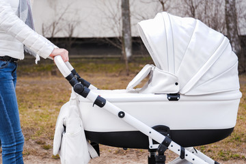 Woman strolling with baby-carriage. Side view.