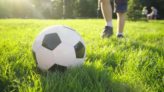 boy puts his foot on a soccer ball. brown shoes. worn sneakers, boots. ball on green grass. children's sport. family holiday. the boy dreams of becoming a famous footballer. training. health. happy 