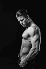 Obraz na płótnie Canvas Muscular model young man on dark background. Black and white fashion portrait of strong brutal guy with modern trendy hairstyle. Sexy naked torso six pack abs. Male flexing his muscles. Sport concept.