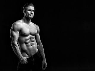 Obraz na płótnie Canvas Muscular model young man on dark background. Black and white fashion portrait of strong brutal guy with modern trendy hairstyle. Sexy naked torso six pack abs. Male flexing his muscles. Sport concept.