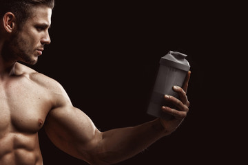 Model sports young man on dark background. Portrait of sporty strong muscle guy with protein drink...