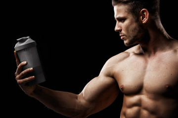 Model sports young man on dark background. Portrait of sporty strong muscle guy with protein drink...