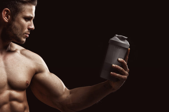 Model sports young man on dark background. Portrait of sporty strong muscle guy with protein drink in shaker. Sexy torso. Bodybuilding nutrition supplements, sport, workout, healthy lifestyle concep.