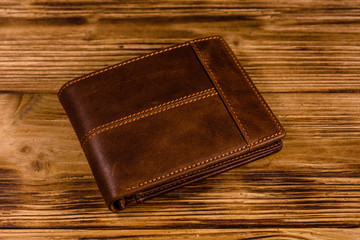 Closed brown leather wallet on wooden table
