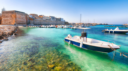 Fototapeta na wymiar Several fishing boats at the Otranto harbour - coastal town in Puglia with turquoise sea