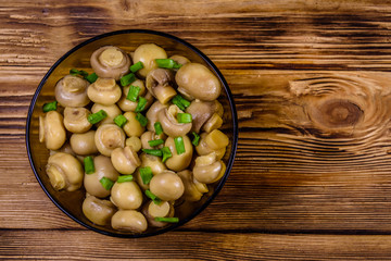Glass bowl with canned mushrooms and green onion on wooden table. Top view