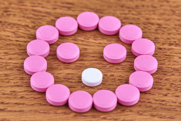 Face made of pink and white pills on wooden background