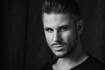 Black and white. Muscular model young man with beard in black t-shirt on dark wooden background. Fashion portrait of brutal sporty sexy strong guy with modern trendy hairstyle. Model, fashion concept.