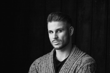 Black and white. Muscular model young man with beard in knitted sweater on dark background. Fashion portrait of brutal sporty sexy strong guy with modern trendy hairstyle. Model, fashion concept.