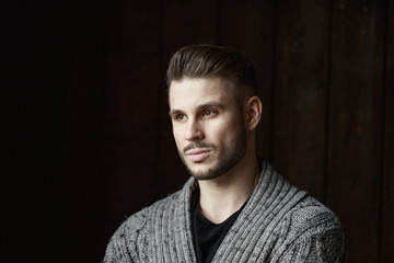 Fototapeta premium Muscular model young man with beard in knitted sweater on dark background. Fashion portrait of brutal sporty sexy strong muscle guy with modern trendy hairstyle. Model, fashion concept.