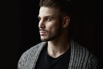 Muscular model young man with beard in knitted sweater on dark background. Fashion portrait of brutal sporty sexy strong muscle guy with modern trendy hairstyle. Model, fashion concept.
