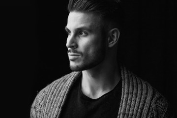 Black and white. Muscular model young man with beard in knitted sweater on dark background. Fashion portrait of brutal sporty sexy strong guy with modern trendy hairstyle. Model, fashion concept.