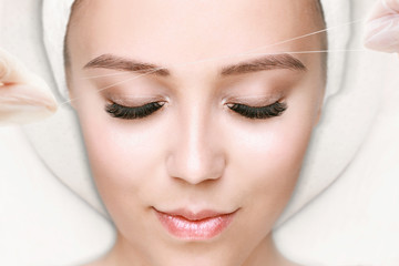 Beautiful young girl tweezing her brows in a beauty salon. Beauty Concept. Cosmetologist plucks...