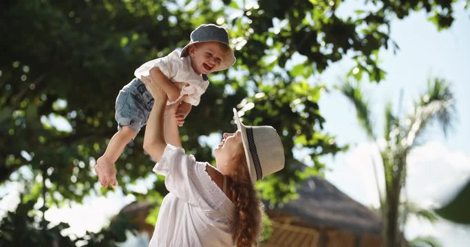 Caucasian mother playing with her adorable baby in tropical garden. Cute child happily smiling and laughing - parenthood, happy childhood concept 4k slow motion