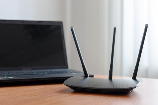 Wireless Wifi Router And Laptop At Wooden Table Indoors. Window Behind. Wireless Connection Concept.