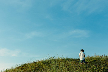 Child on top of a hill exploring on its own new horizons, blue sky copy space.