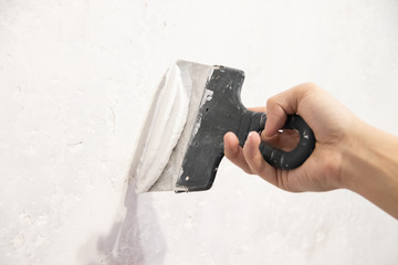 Male hand with a spatula putty wall. . Align the wall. White wall. Putty on the wall