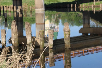 Wodden posts of old broken bridge near modern construction with church reflection in river water