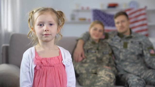 Joyful parents in US military uniform admiring little daughter looking at camera