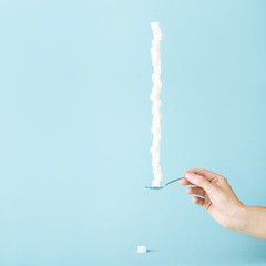 Female hand holding a spoon with column made of sugar cubes Sweet life concept.