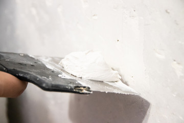 Male hand with a spatula putty wall. . Align the wall. White wall. Putty on the wall