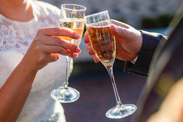 Dating or wedding concept - couple drinking white wine or champagne outdoors. A young couple clink glasses with an alcoholic drink. Sun glare in the glasses.