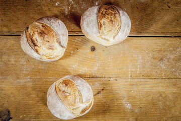Three small loafs of French bread on display on a rustic wooden table, baguette style. They are called in French petits pains, made of yeast called levain