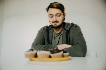 Fototapeta na wymiar A young hipster on a diet with cupcakes