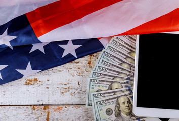 Hundred US dollar bills above digital tablet US flag.