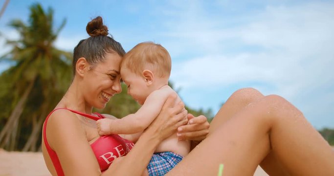 Mom with a baby sitting on the sand on the beach hugs and kisses the child. in slow motion
