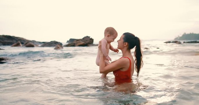 Mom with 6 month old son bathes in the ocean. The family found quiet water and sits in a natural pool. real time