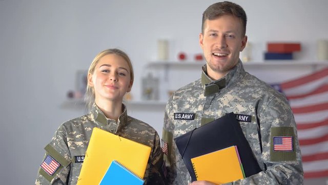 Female and male US military students with folders smiling at camera, education