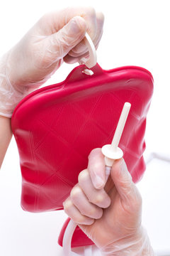 Nurse wearing sterile rubber gloves holds Cleansing Enema Bucket Set on white background. Enema Mug of Esmarch.
