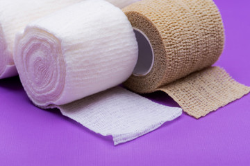 Fototapeta na wymiar Hospital Grade Sterile Rolled Gauze and Elastic Self-Adhering Compression Bandage (Cohesive Bandage) on purple background.