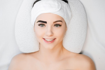 Beautiful young girl with long eyelashes tweezing her eyebrows in a beauty salon. Woman doing eyebrow permanent makeup correction . Microblading brow.