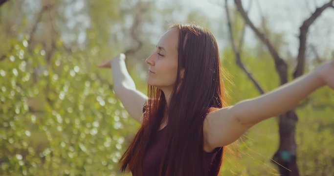 Young woman enjoys nature in the forest, raises her hands up from pleasure. Sunny spring day. Portrait view.