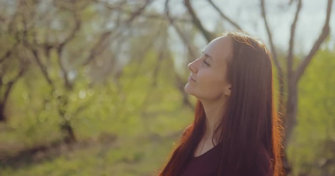 Young happy woman walks in the spring forest and enjoys the weather. Brunette girl is smiling. Portrait view.