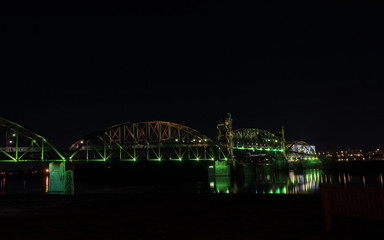 Bridge with colorful lighting at night and park bench in foreground