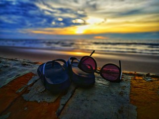 Beautiful sunset view with flip-flop and sunglasses on beach background.