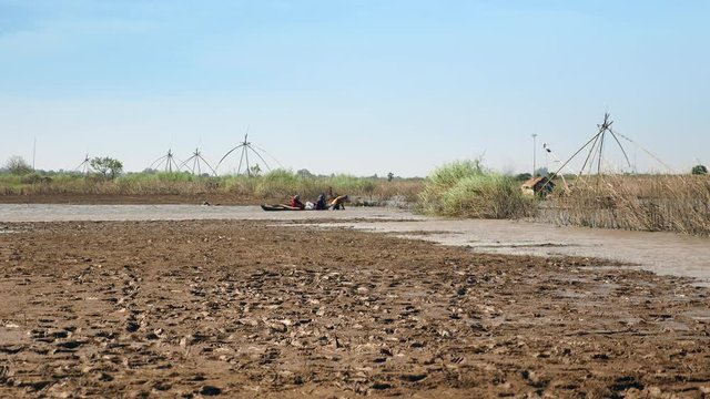  people digging for clams on lake. Chinese fishing nets as backdrop