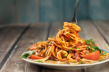 plate of pasta seasoned with herbs, tomatoes and sauce on a wooden table close-up, fork with long pasta and sauce, share menu restaurant and cafe