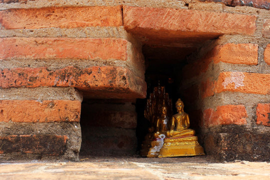 Small golden buddha statues hidden in a red brick wall.