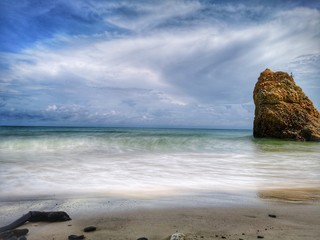 Beautiful single rock formation on the seashore with silky smooth water reflection background.