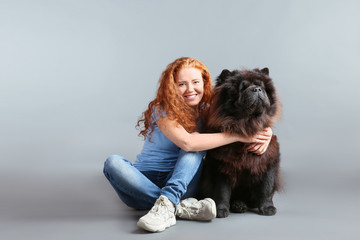 Young woman with cute Chow-Chow dog on grey background