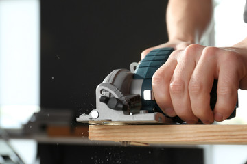 Male carpenter using electric cutter in workshop, closeup