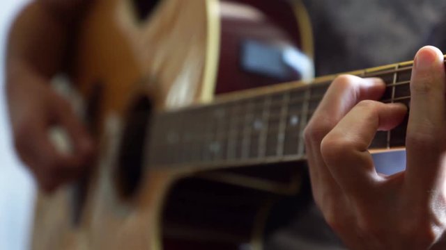 Guitarist playing acoustic guitar in studio - selective focus close-up of the fingerboard and hand playing rock pop chords