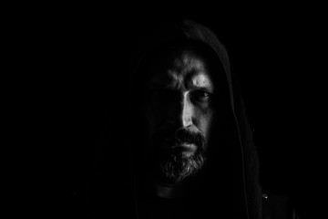 Brutal man with a gray beard in the hood with sharp shadows on a black background. Copy space.