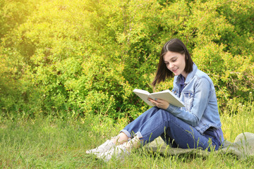 Naklejka na ściany i meble Beautiful young woman reading book in park