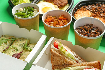 Containers with delicious food on color background