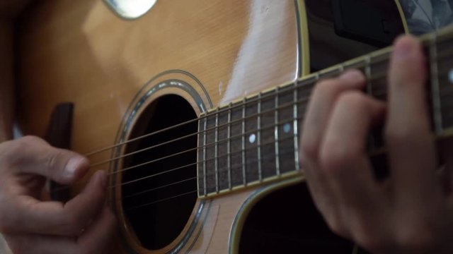 Guitarist playing acoustic guitar in studio - selective focus close-up of the fingerboard and hand playing rock pop chords